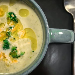 Broccoli cheddar soup in a green mug with a silver spoon on a dark background.
