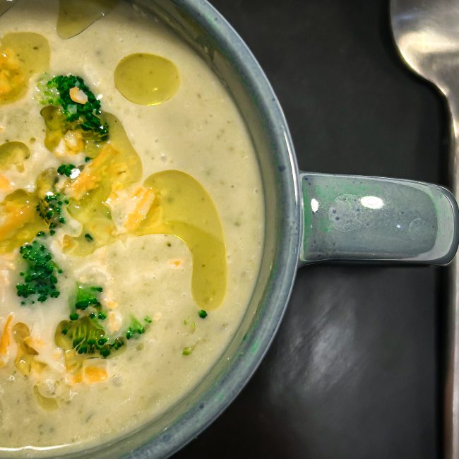 Broccoli cheddar soup in a green mug with a silver spoon on a dark background.