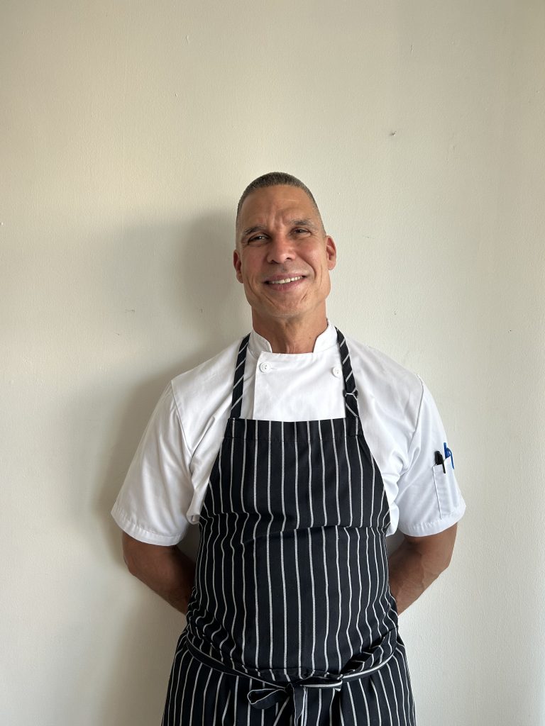 Chef standing on a white background in white chef's uniform and a striped apron.